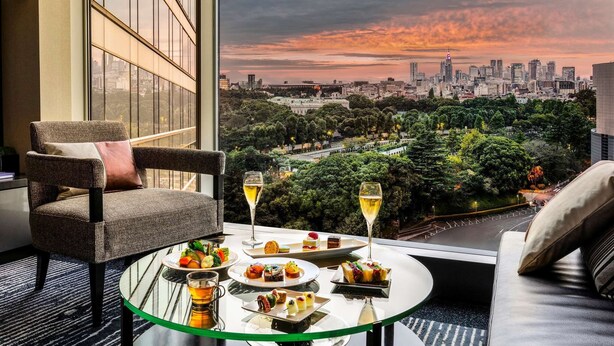 Un balcón con una mesa lista para comer, con vistas a un paisaje urbano al atardecer.
