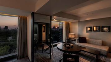 A modern hotel room with a city view, a round dining table, a sofa, and a small side table.
