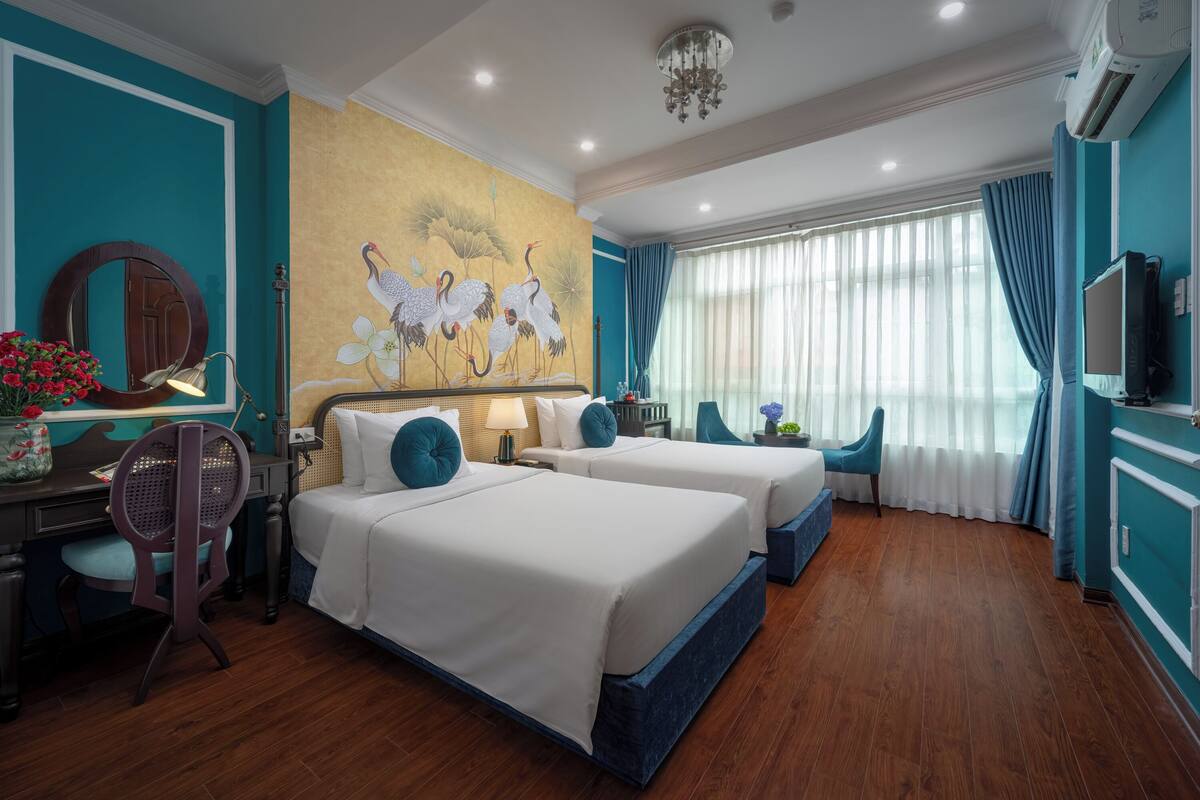 Une chambre d’hôtel avec deux lits, un bureau, une chaise, une télévision et une fresque murale.