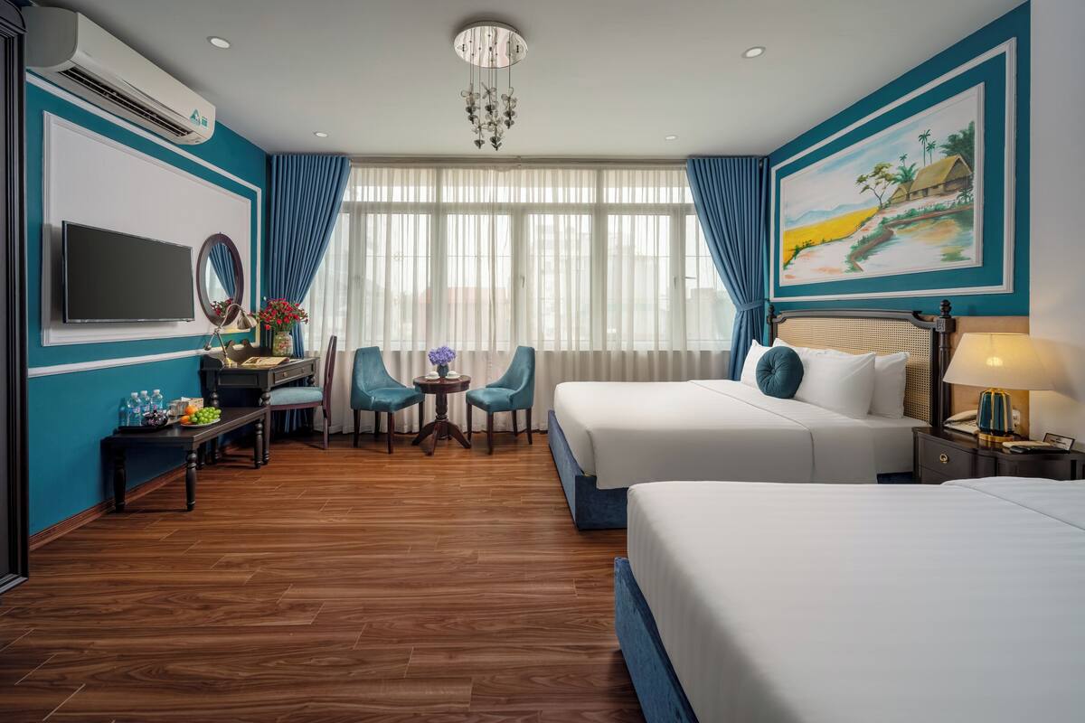 Une chambre d’hôtel avec deux lits, un bureau avec une chaise, une télévision et un tableau au mur.