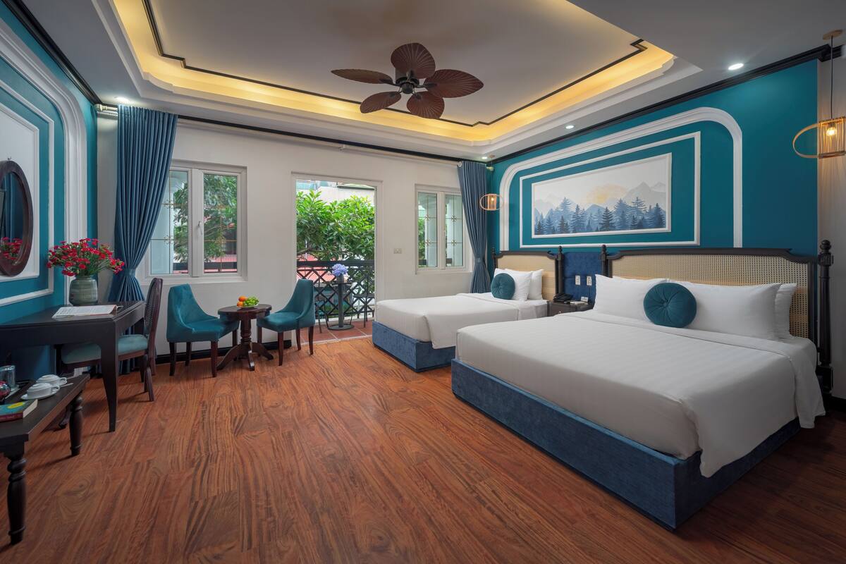 Une chambre avec deux lits, un coin repas comprenant une table et des chaises, un ventilateur de plafond et une vue sur la verdure environnante.