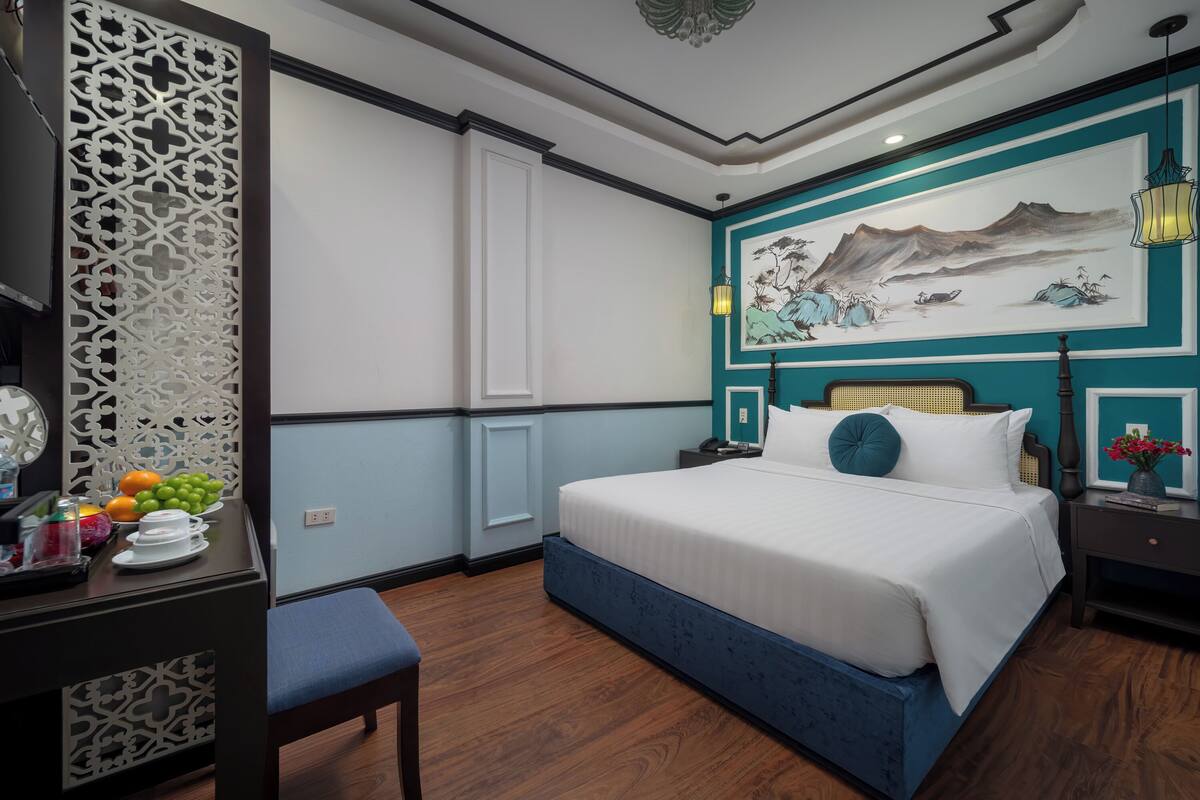 Une chambre à coucher avec un lit, un bureau sur lequel se trouvent des fruits, un paravent décoratif et un tableau accroché au mur.