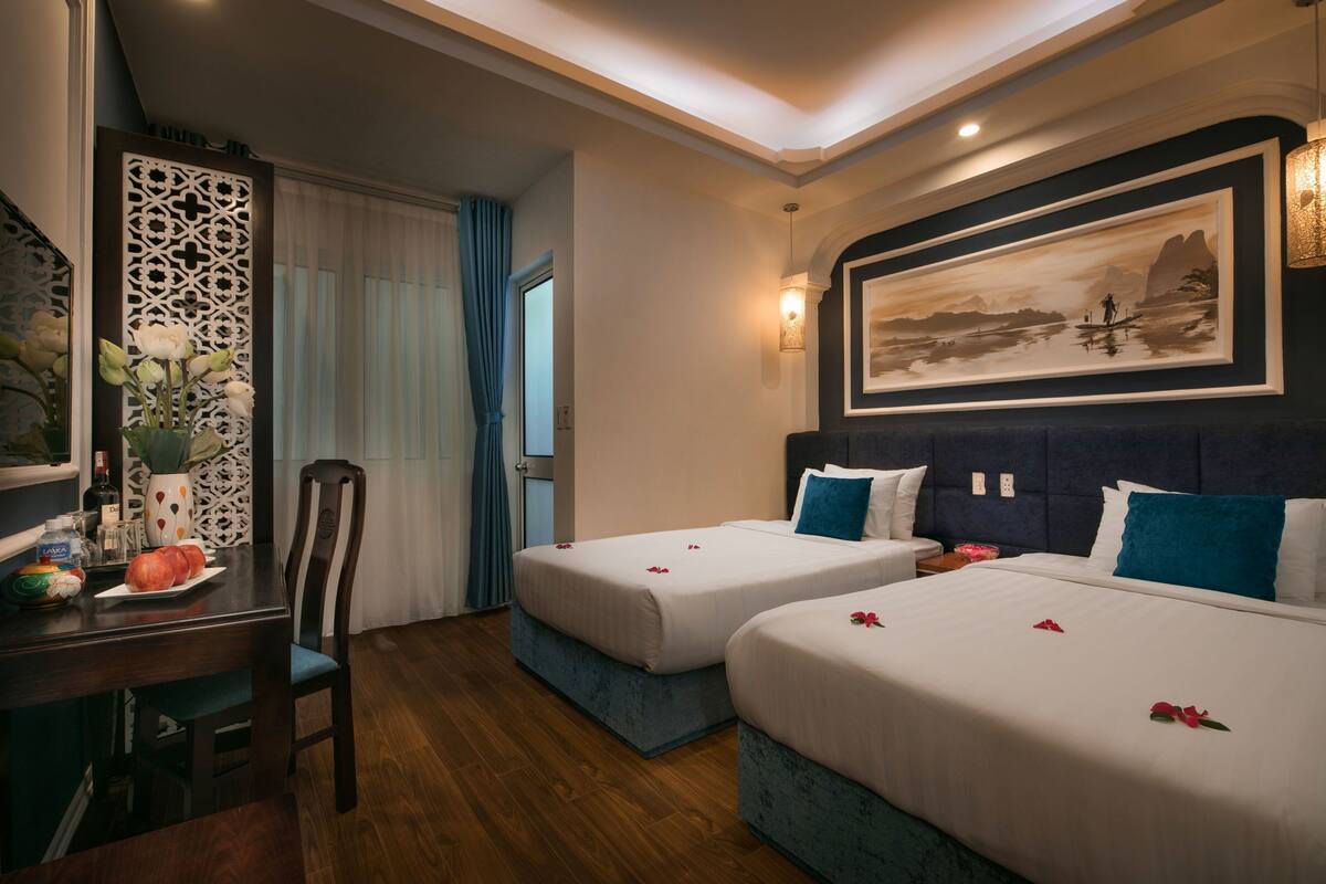 Une chambre d’hôtel avec deux lits, une table à manger, un panneau décoratif mural et une œuvre d’art encadrée.