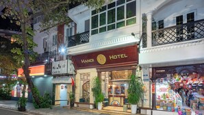 Un hôtel avec une enseigne indiquant « HÔTEL DE HANOÏ » et une entrée bien visible, agrémentée de plantes en pot.