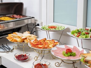 Un bufé con diversas opciones de comida, incluyendo pan, pizza, ensaladas y carnes.