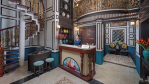 Un espace d’accueil comprenant un bureau de réception, un comptoir d’information touristique et un guichet. On y trouve également un escalier avec des rampes décoratives et un lustre.