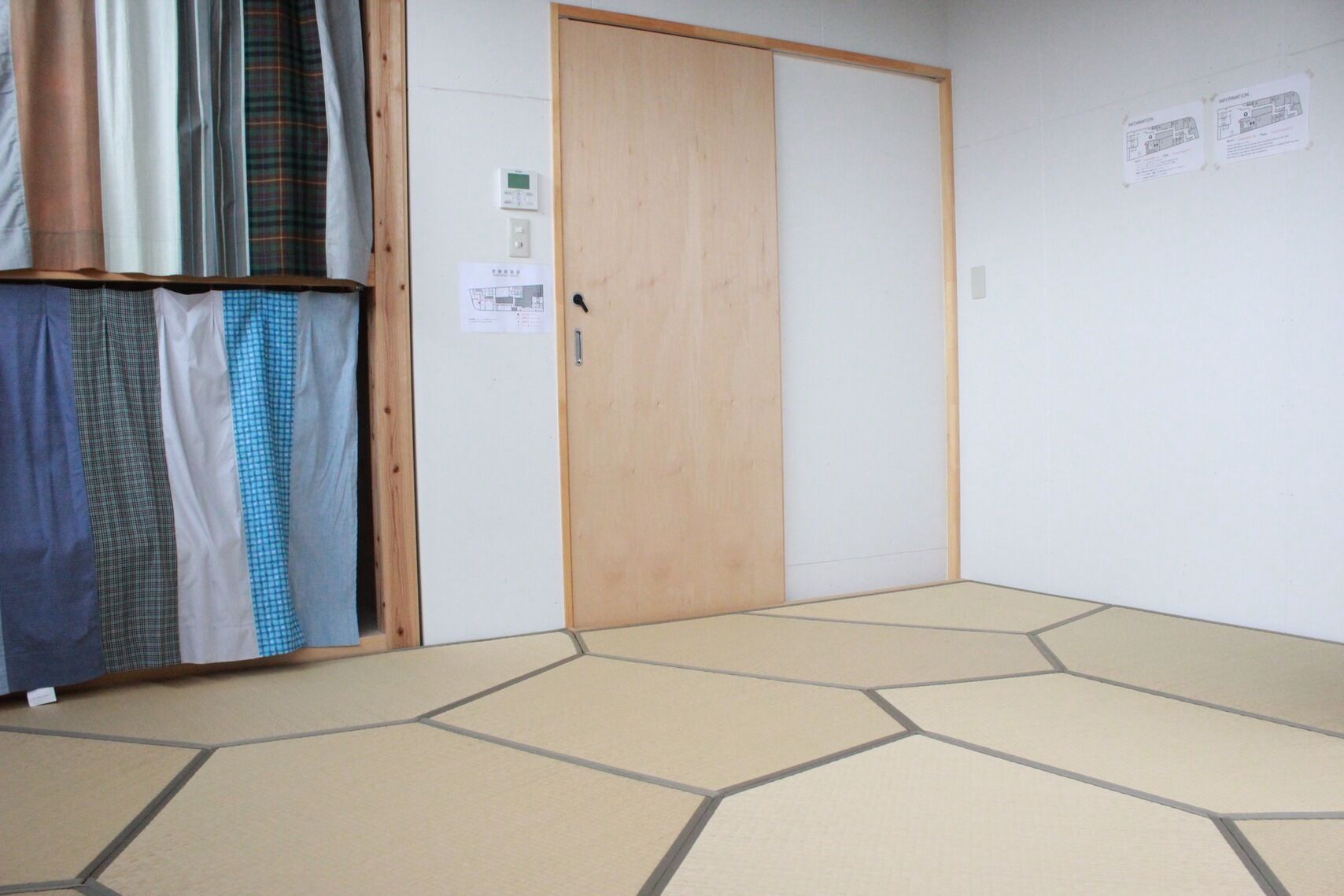 A room with a wooden door, a tiled floor, and a wall with two informational posters.