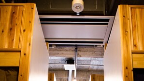 A corridor with wooden paneling and a white floor, leading to a room with a concrete wall and a circular window. - Hostel and Dining Tanga Table (Kitakyushu)