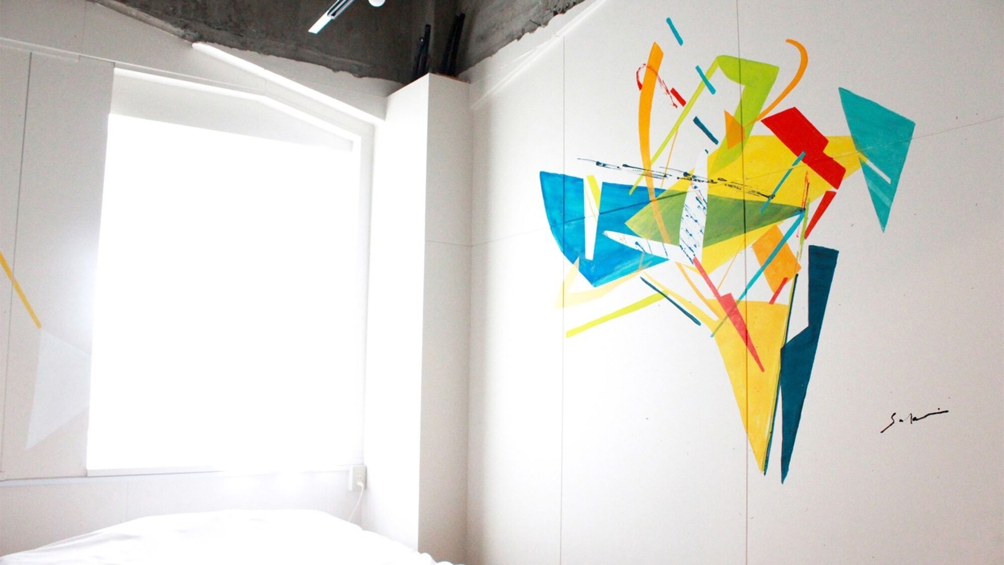 A room with a bed, a window, and a colorful abstract wall art.