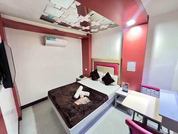 Habitación de hotel con cama, escritorio, silla, televisor y aire acondicionado instalado en la pared.