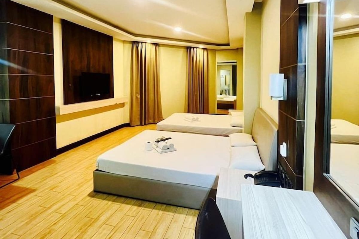 A hotel room with a wooden floor, two beds, a TV, a desk, and a mirror.