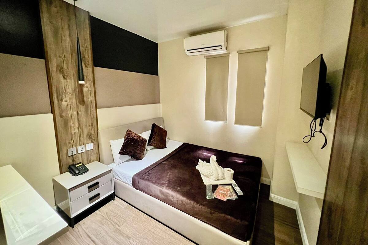 Un dormitorio moderno con cama, mesitas de noche, escritorio, aire acondicionado y televisor.