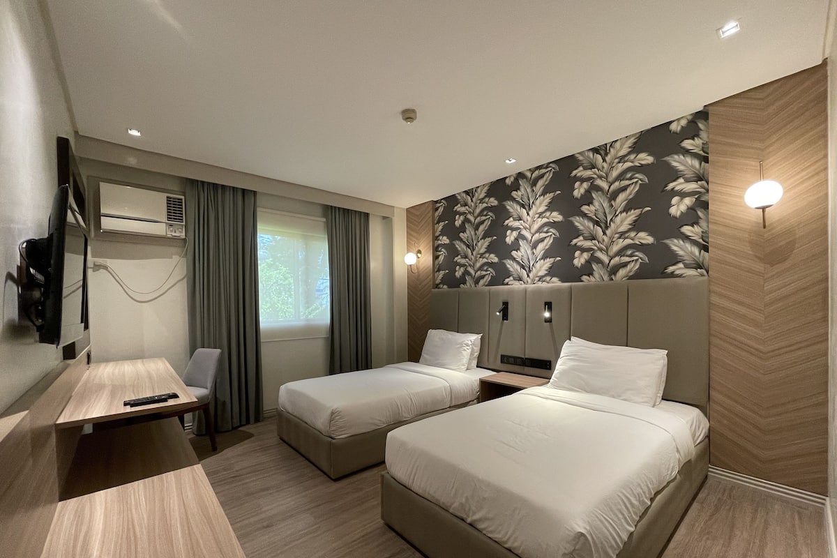 Habitación de hotel con dos camas, un escritorio, un televisor y una ventana con cortinas.