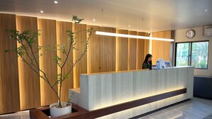 Una recepción con recepcionista, paredes de paneles de madera, una planta en maceta y un reloj en la pared.