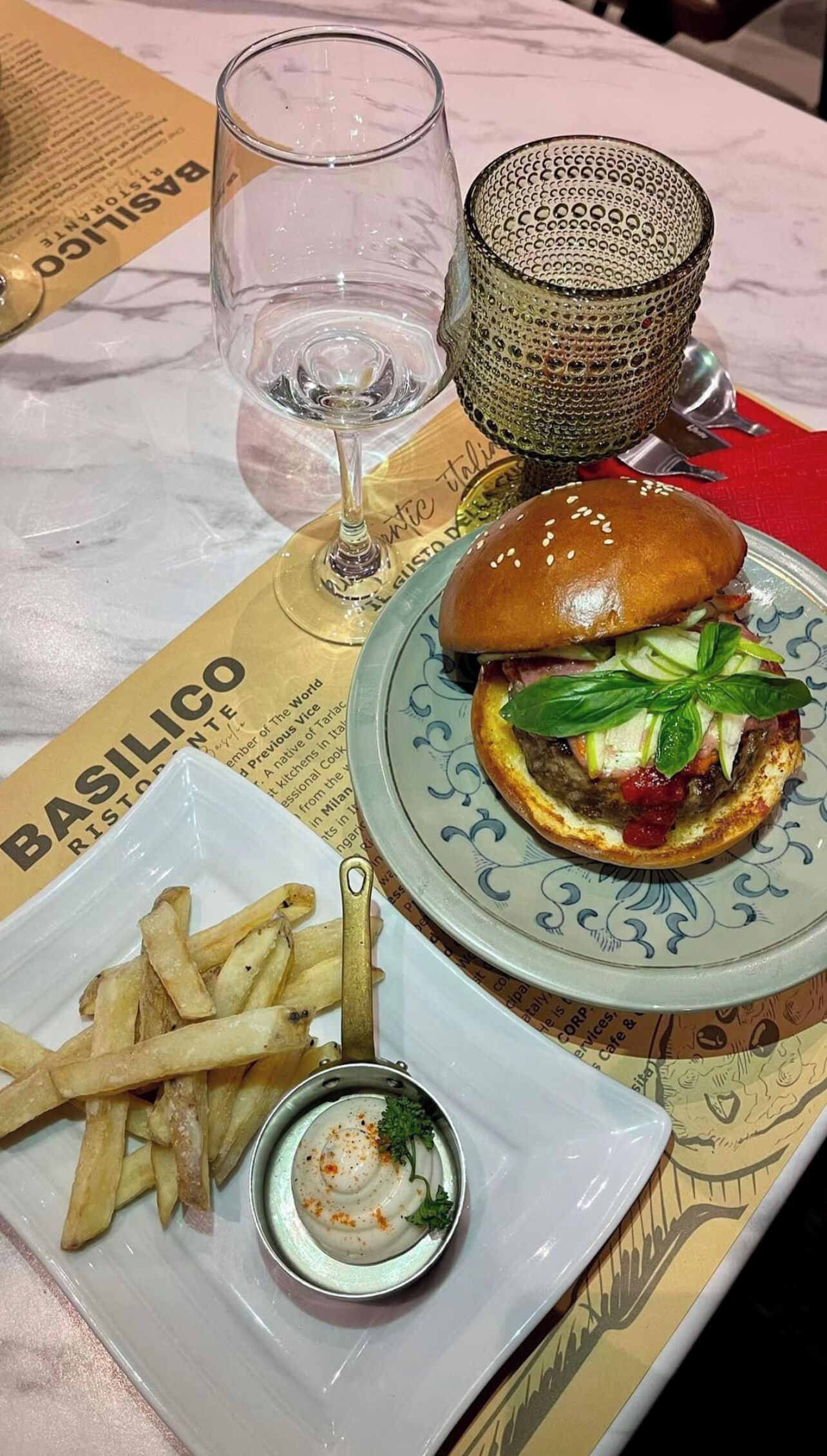A meal with a burger, fries, and a small cup of sauce on a table with a menu.