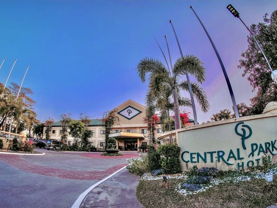 A hotel entrance with a sign reading "Central Park Hotel," surrounded by palm trees and a clear sky.