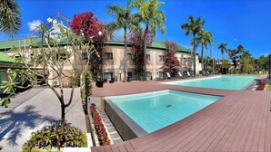 Una piscina con cubierta de madera, rodeada de palmeras y sillones de descanso.