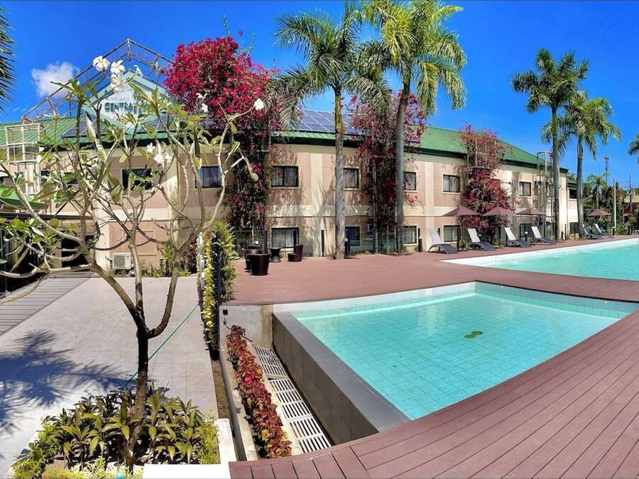 Una piscina con cubierta de madera, rodeada de palmeras y sillones de descanso.