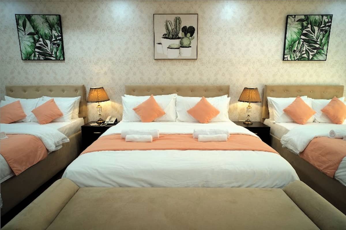 Una habitación de hotel con una cama grande, dos mesitas de noche y una mesita auxiliar. Hay dos lámparas de pared a cada lado de la cama.