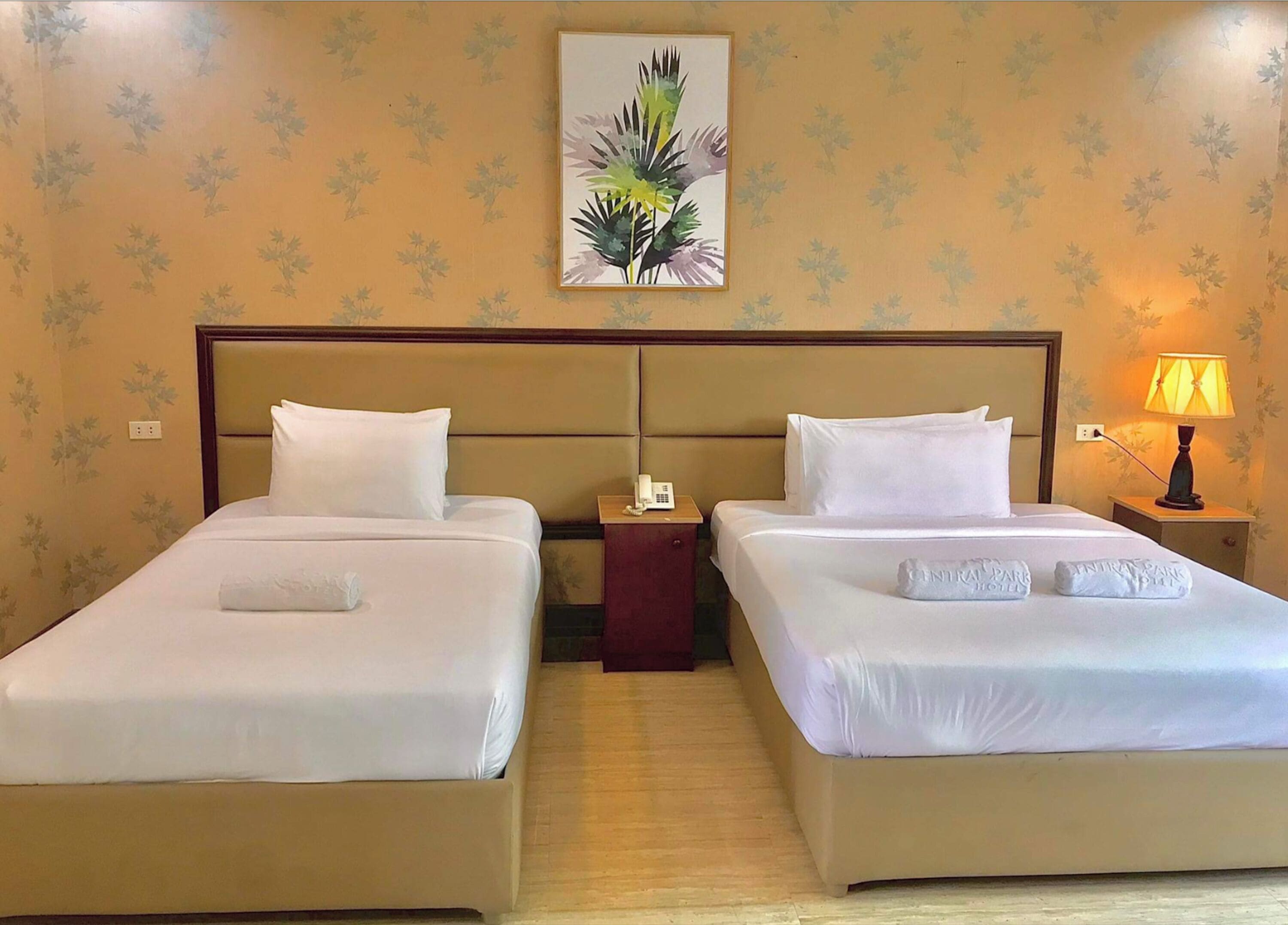 Een hotelkamer met twee bedden, een nachtkastje met een lamp, en een bloemenpatroon op de muur.