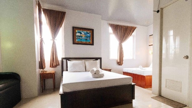 A hotel room with a bed, a nightstand, a painting, a window, and a bathroom. - Getz Hotel (Manila)