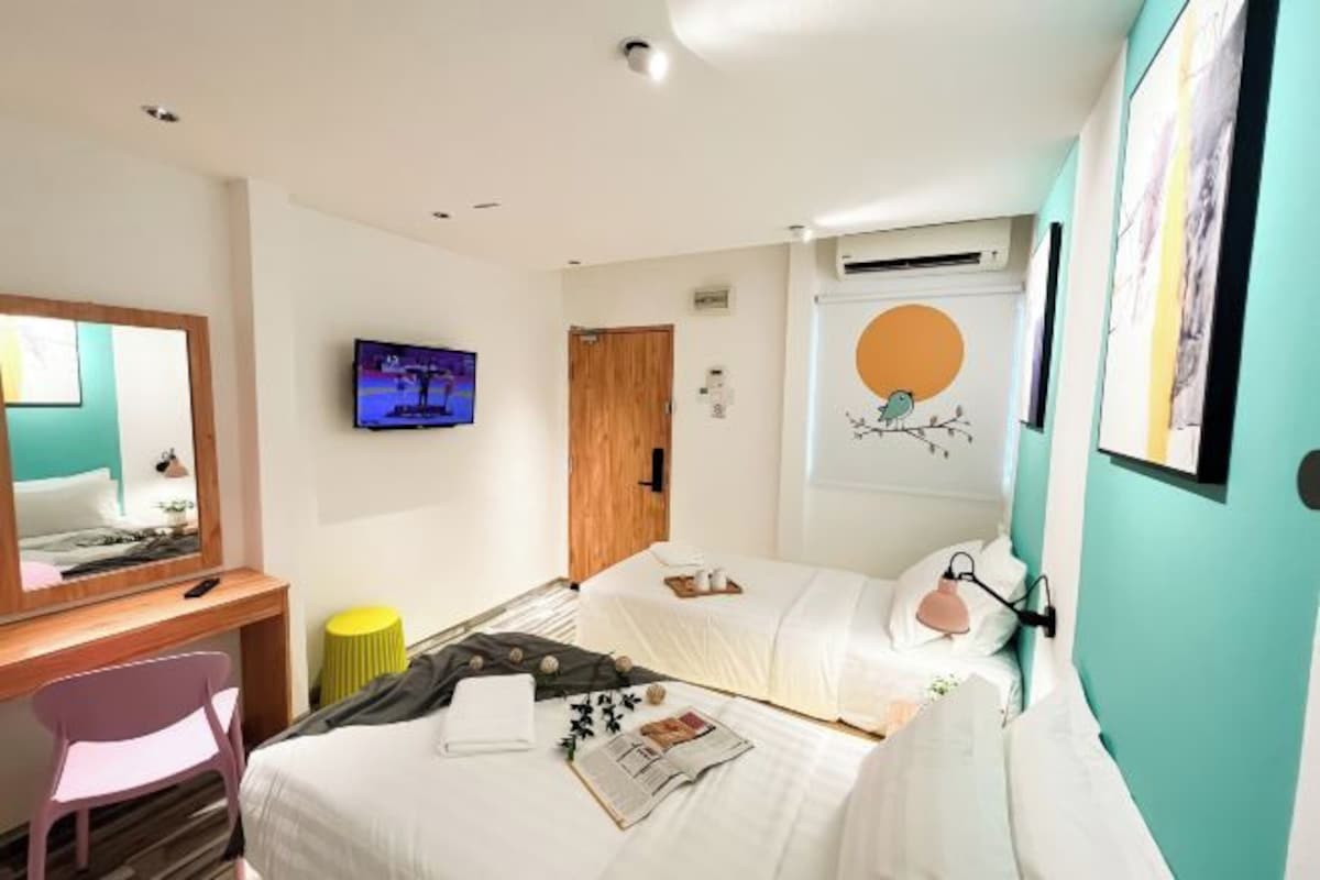 A hotel room with two beds, a desk, a chair, a TV, and a wall-mounted artwork.
