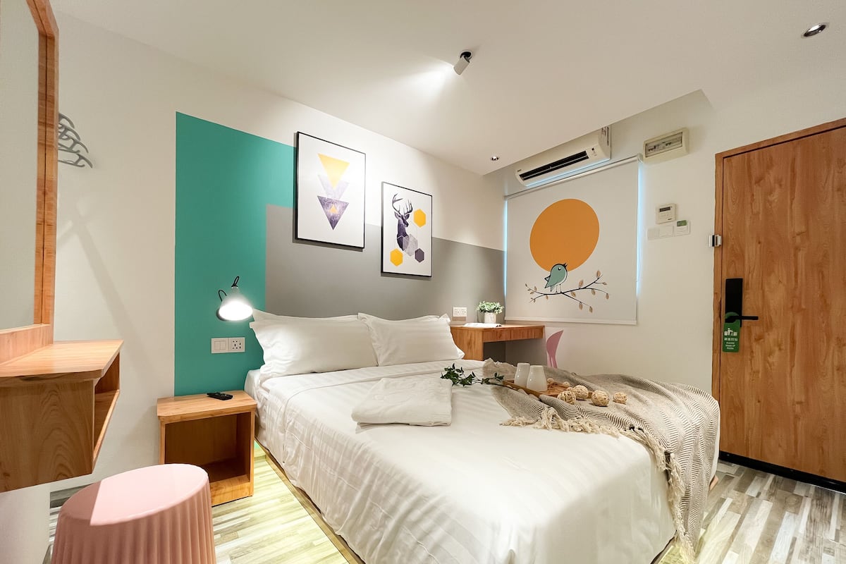 A modern bedroom with a bed, bedside tables, a nightstand, a wall-mounted lamp, and artwork.