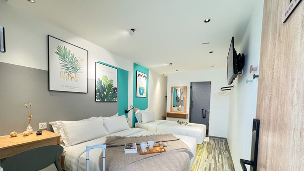 A hotel room with two beds, a desk, a chair, a suitcase, and a bathroom with a mirror and a shower. - Apple 1 Hotel Gurney (George Town)