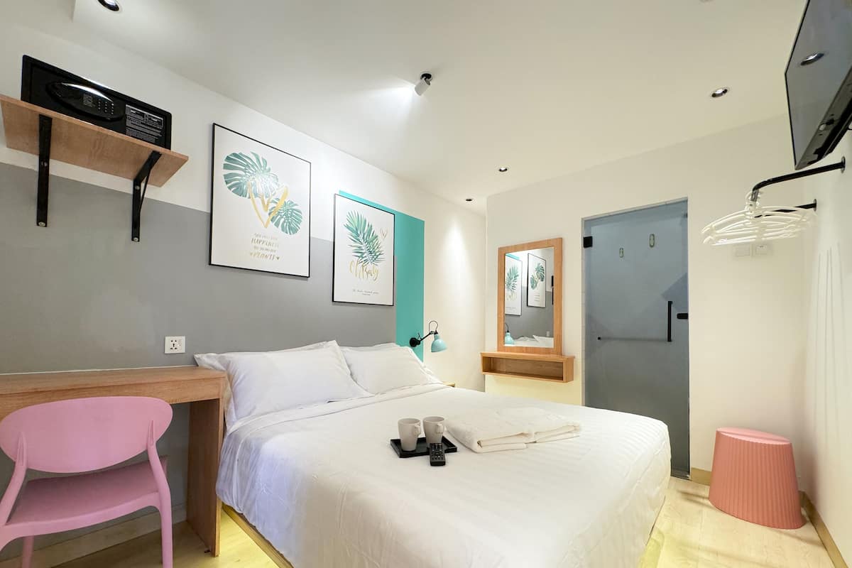 A hotel room with a bed, a desk, a chair, a mirror, and a door.