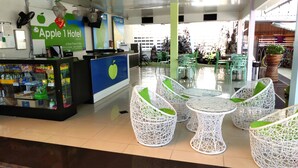 A hotel reception area with a counter, a fruit stand, and wicker chairs around a glass table. - Apple 1 Hotel Gurney (George Town)