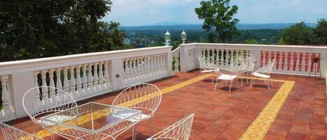 A terrace with white metal chairs and a table, overlooking a scenic landscape.