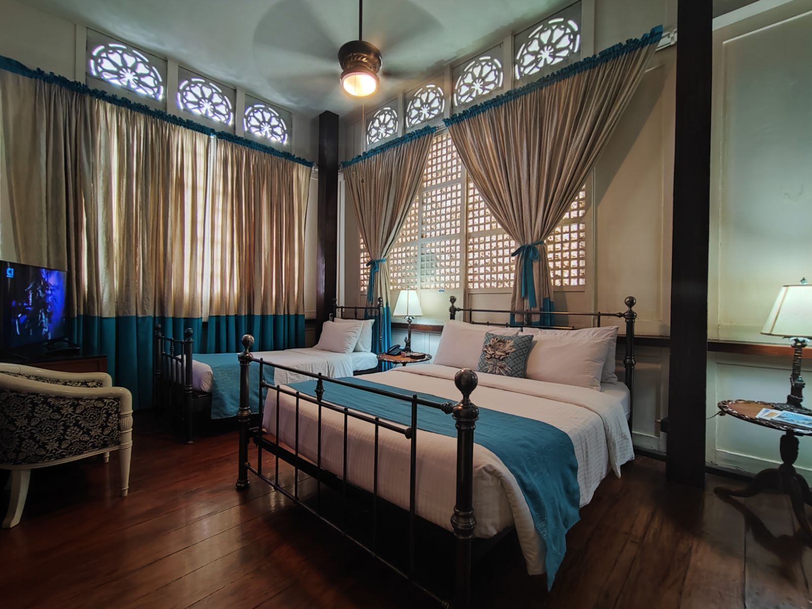 Une chambre d’hôtel avec deux lits, une télévision, une petite table et une fenêtre agrémentée de rideaux décoratifs.