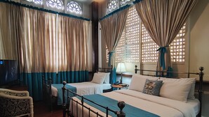 A bedroom with two beds, a wooden floor, a ceiling fan, and a TV. - Paradores Del Castillo (Taal)