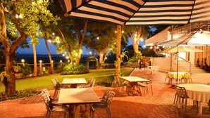 An outdoor patio with tables and chairs, string lights, and a view of the ocean at dusk. - Paradores Del Castillo (Taal)