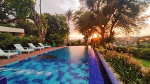 A swimming pool with blue tiles, surrounded by greenery and trees, with a sunset in the background. - Paradores Del Castillo (Taal)