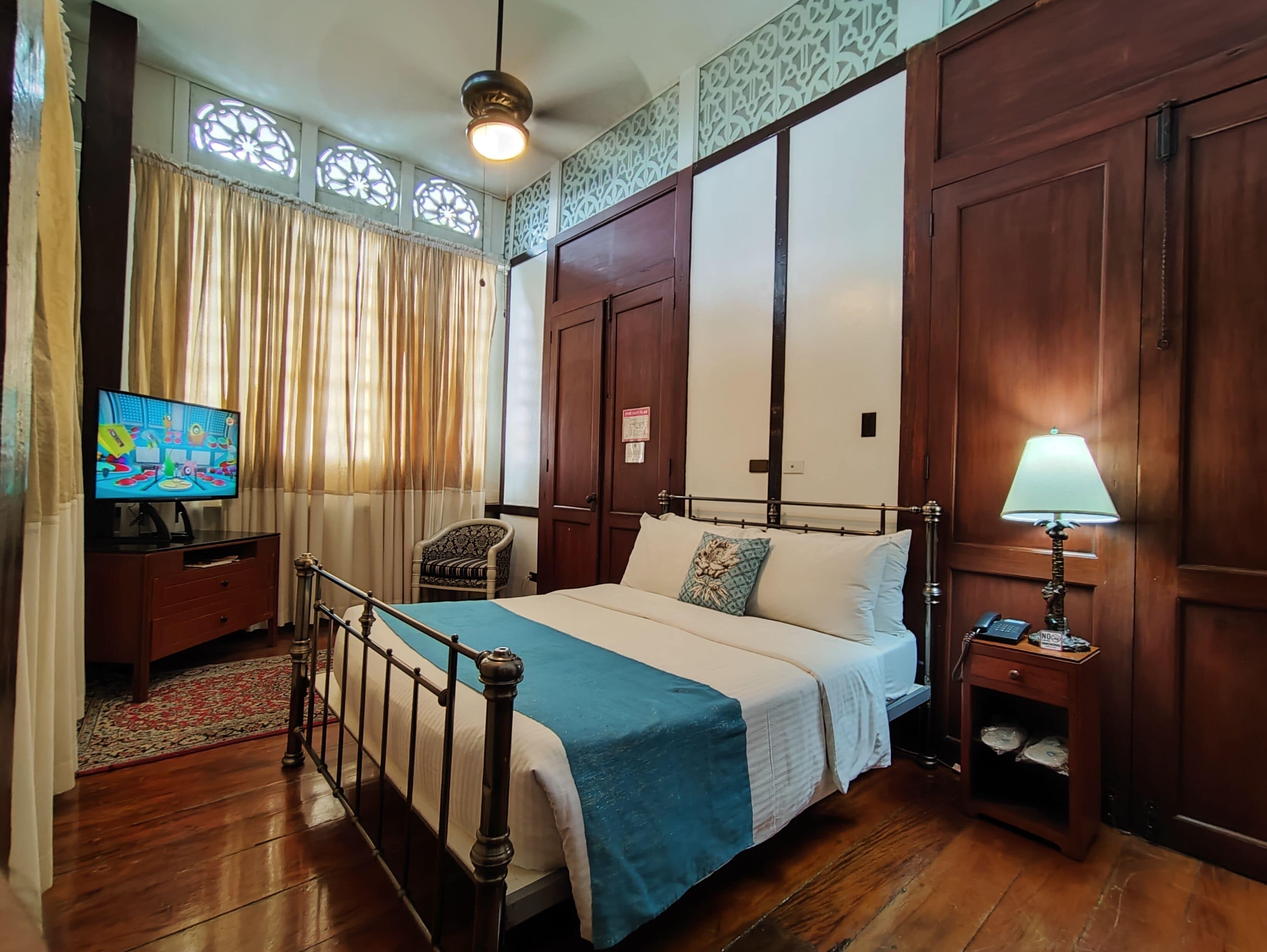 A bedroom with a bed, a television, a chair, a nightstand, and a lamp.
