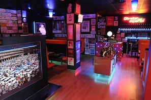 A bar area with a neon sign reading "Gibraltar espanol," framed pictures on the walls, and a large display of cars. - Resotel (Villares de la Reina)
