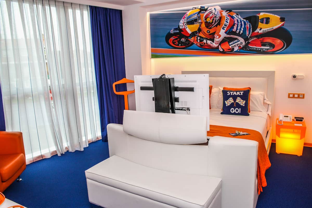 Una habitación de hotel con una cama grande, un sofá blanco, un televisor y un cartel de una motocicleta en la pared.