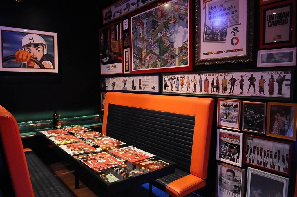 Una habitación con un banco acolchado negro, una mesa con revistas y varias fotografías enmarcadas en las paredes.