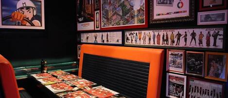 Una habitación con un banco acolchado negro, una mesa con revistas y varias fotografías enmarcadas en las paredes.