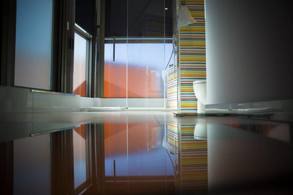 Habitación de hotel moderna con un ventanal grande, pared a rayas y suelo reflectante.