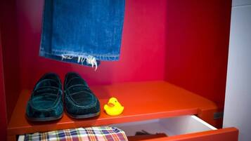 Una habitación infantil con una pared roja, un par de pantuflas azul oscuro, un patito de goma amarillo y un tejido escocés en el suelo.