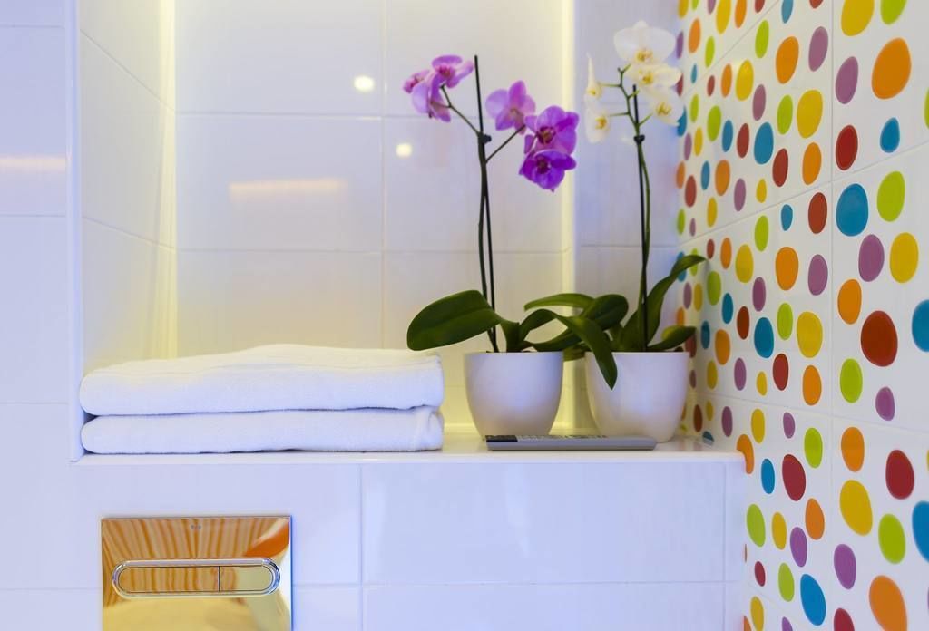 A bathroom with white tiles, a towel rack, and two potted plants with flowers.