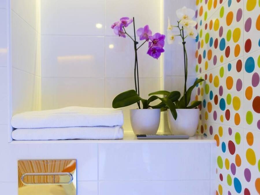 A bathroom with white tiles, a towel rack, and two potted plants with flowers.