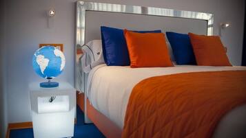 A neatly made bed with a white headboard, blue and orange pillows, and a globe on a bedside table.