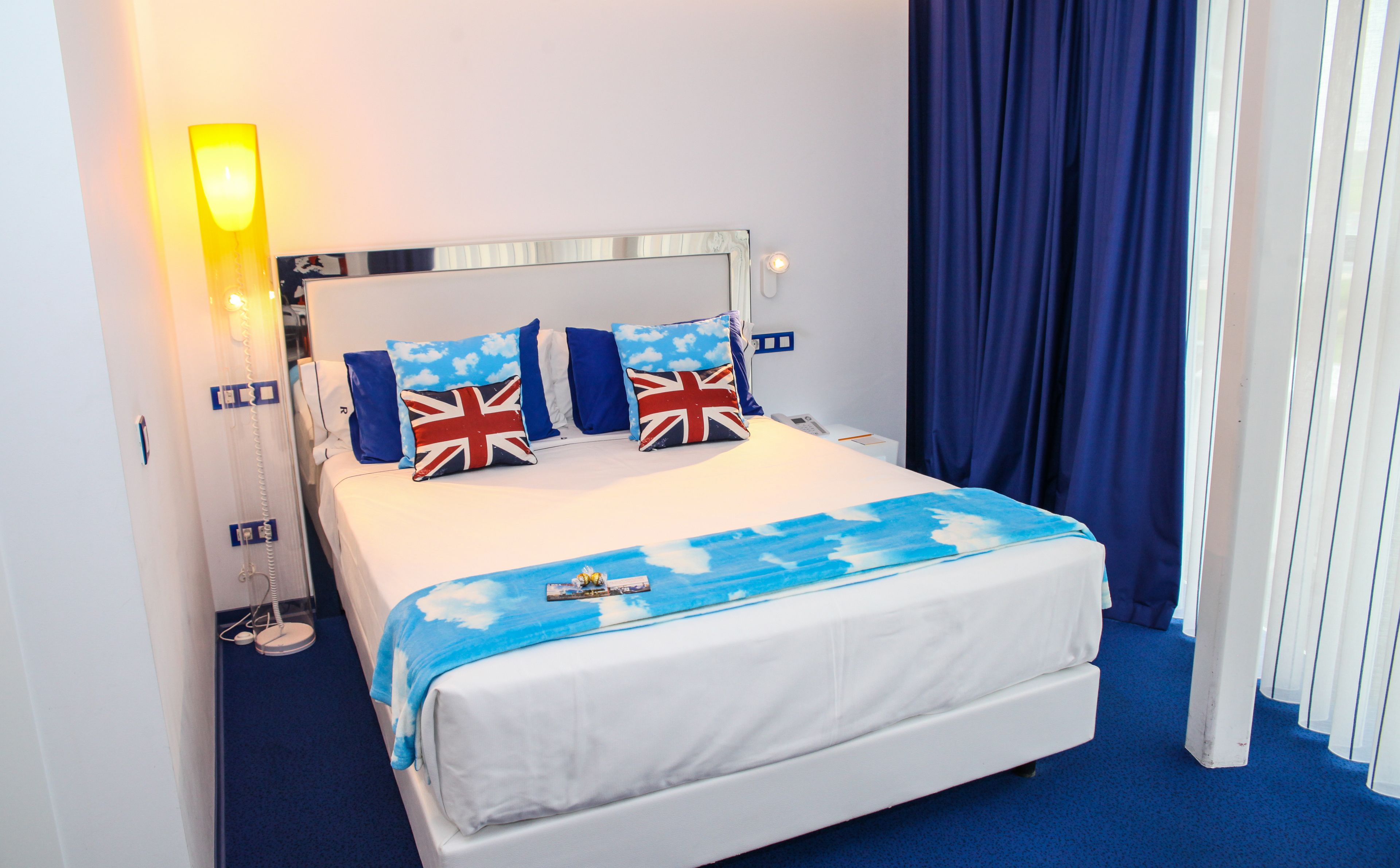 A neatly made bed with a white mattress and blue bedding, featuring pillows with the Union Jack design.