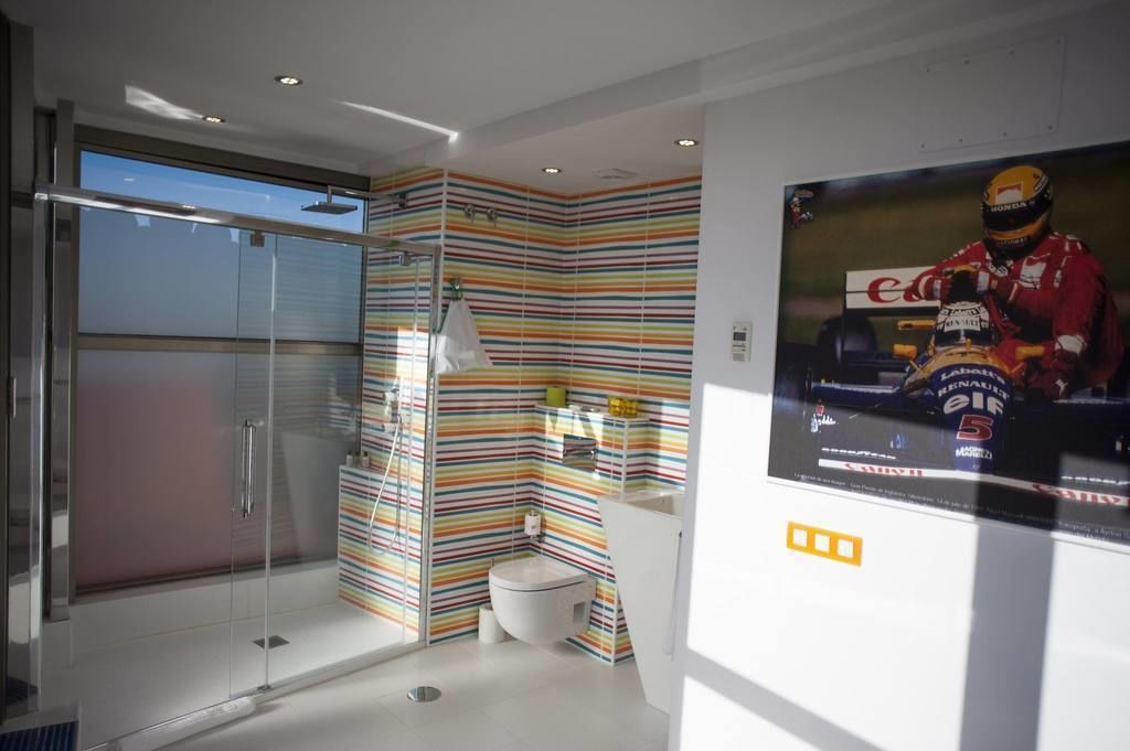Une salle de bain moderne avec une douche à parois de verre, un motif rayé sur un mur et une affiche représentant un pilote de course.