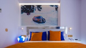 Un dormitorio con cama, almohadas, un globo terráqueo y un televisor que muestra un paisaje nevado con un automóvil.