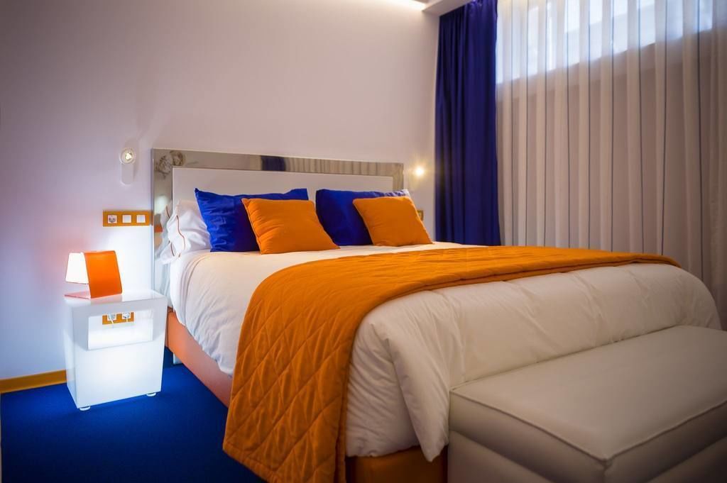 Una habitación de hotel con una cama, una mesita de noche, una lámpara y una ventana con cortinas.