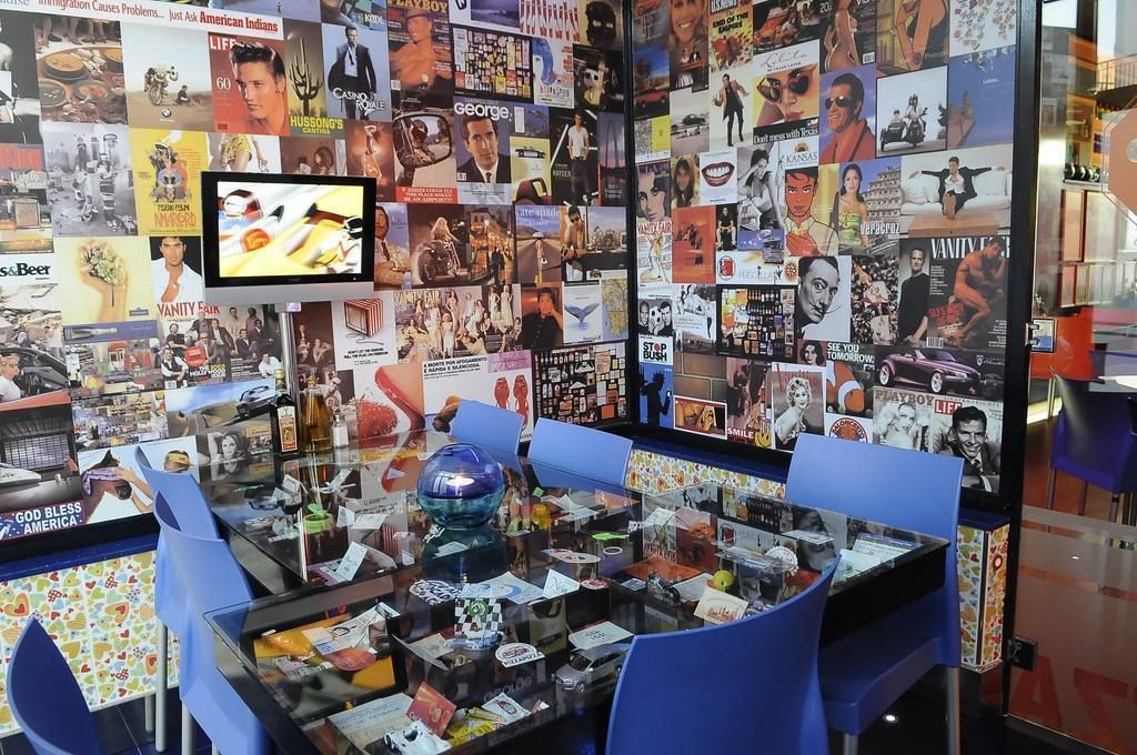 A room with a glass table displaying various items, surrounded by blue chairs.